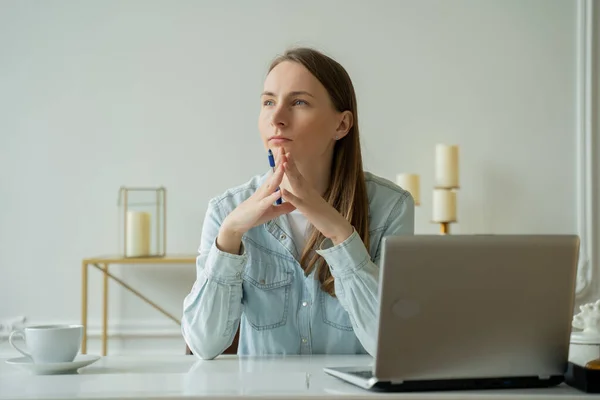 Mujer joven que trabaja en el ordenador portátil y mira cuidadosamente a la distancia mientras está sentada en su lugar de trabajo en la oficina — Foto de Stock