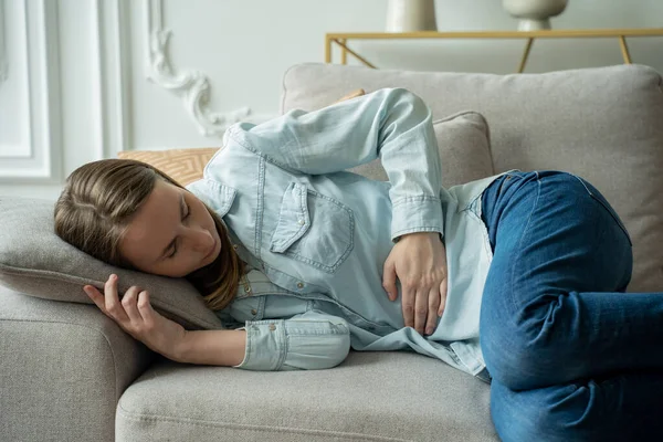 Mujer joven que sufre de dolor abdominal mientras está sentada en el sofá en casa — Foto de Stock