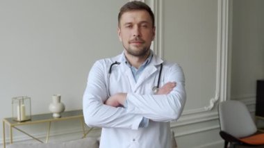 Beyaz laboratuvar önlüklü ve boynunda steteskop olan bir doktorun portresi. Kolları göğsünde, kameraya bakıyor.