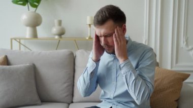 Evde kanepede otururken baş ağrısından muzdarip genç adam kafasına dokunuyor.