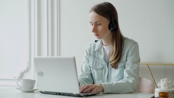 Femme parlant dans une vidéoconférence en ligne avec un casque avec microphone et utilisant un ordinateur portable au bureau, consultant client — Video