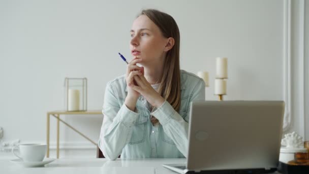 Mujer joven que trabaja en el ordenador portátil y mira cuidadosamente a la distancia mientras está sentada en su lugar de trabajo en la oficina — Vídeos de Stock