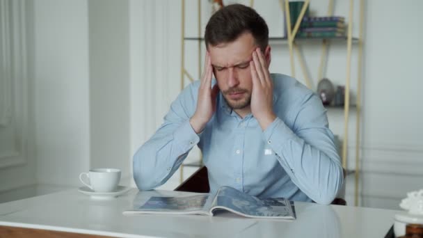 Een trieste jongeman met hoofdpijn zit aan een bureau in het kantoor. — Stockvideo
