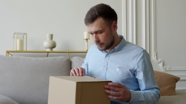 Man öppnar en paketlåda hemma medan man sitter på soffan — Stockvideo