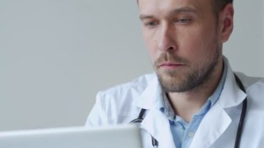 Ofiste dizüstü bilgisayarla çalışan yakın çekim odaklı bir doktor. Klinikteki masada dizüstü bilgisayar kullanan erkek doktor.