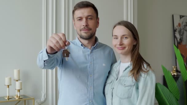 Ευτυχισμένο ζευγάρι νέων δείχνουν νέα κλειδιά του σπιτιού. Νεαρό χαμογελαστό ζευγάρι που δείχνει τα κλειδιά για το νέο σπίτι αγκαλιάζει κοιτάζοντας κάμερα. — Αρχείο Βίντεο