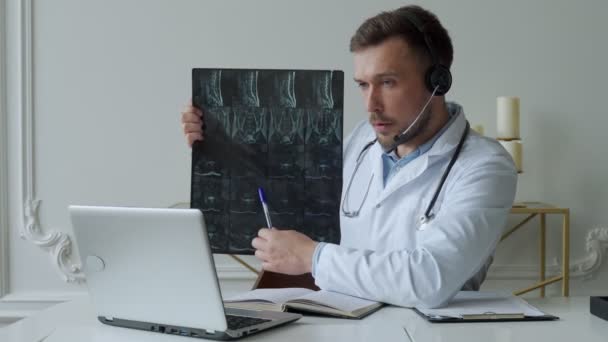 Médecin masculin à l'écoute du patient pendant la séance de télémédecine. Homme médecin ayant une consultation en ligne sur ordinateur portable tenant l'image radiographique et discuter du diagnostic — Video