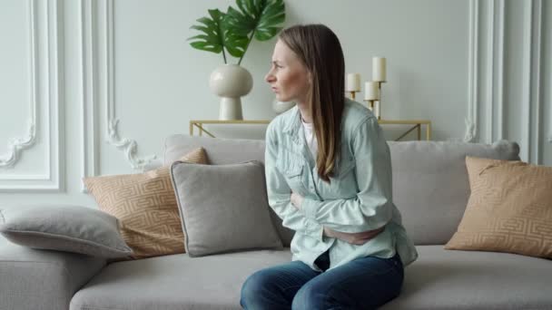 ผู้หญิงสาวทุกข์ทรมานจากอาการปวดท้องขณะนั่งบนโซฟาที่บ้าน — วีดีโอสต็อก