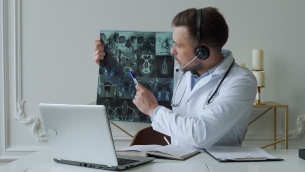 Teletıp seansı sırasında hastayı dinleyen erkek doktor. Adam doktor bilgisayarında röntgen görüntüsü tutuyor ve teşhisi tartışıyor. — Stok video