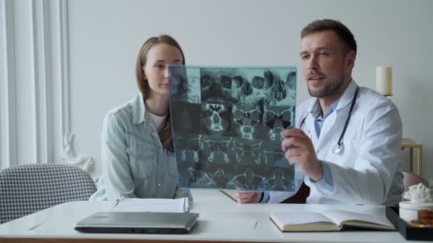 Mężczyzna lekarz pokazać wyniki rentgenowskie i wyjaśnić problemy zdrowotne do kobiet pacjenta w jego biurze — Wideo stockowe