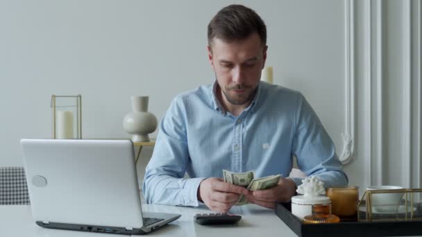 Człowiek z pieniędzmi i kalkulatorem sprawdza rachunki, oblicza wydatki, bada saldo kredytowe siedząc przy stole w domu — Wideo stockowe