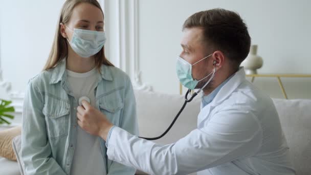 Mannelijke arts luistert naar het hart en de longen van een vrouwelijke patiënt tijdens het zitten op de bank — Stockvideo