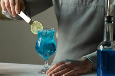 Blue Lagoon barında barmen kokteyli hazırlıyor. Adam limonla kokteyl süslüyor.