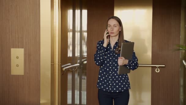 Mujer de negocios en cámara lenta en una camisa sale del ascensor y habla en un teléfono móvil — Vídeos de Stock