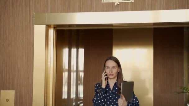 Mujer de negocios en cámara lenta en una camisa sale del ascensor y habla en un teléfono móvil — Vídeos de Stock