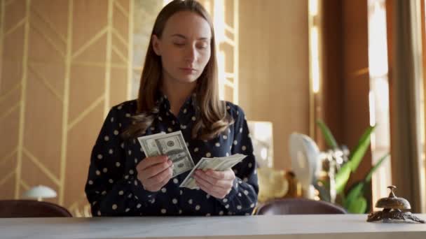 Vrouw in shirt telt dollars geld in haar handen zittend op een stoel — Stockvideo