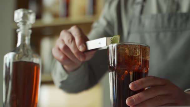 Profesyonel bir barmen kokteyli limonla süslüyor. Barmen viski ve kolayla bir kokteyl hazırlıyor. Barda kokteyl hazırlıyorum.. — Stok video