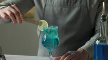 Blue Lagoon barında yakın plan bir barmen hazırlanıyor. Adam limonla kokteyl süslüyor.
