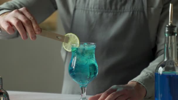 Barman z bliska przygotowuje przy barze koktajl Blue Lagoon. Mężczyzna ozdabia koktajl limonką — Wideo stockowe