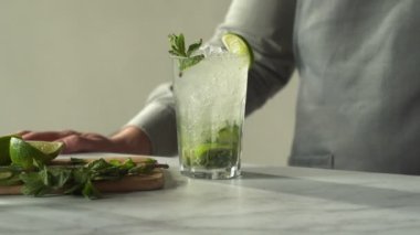 Barmen barda mojito kokteyli hazırlıyor. Bir adam mojito kokteylini nane ve limonla süslüyor.
