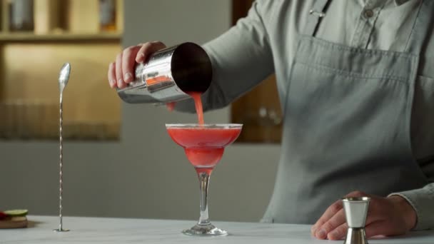 Barkeeper gießt einen Cocktail in ein Margarita-Glas, dekoriert das Glas mit Limette und Erdbeeren — Stockvideo