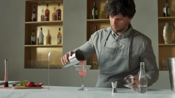 Barkeeper gießt einen Cocktail in ein Margarita-Glas, dekoriert das Glas mit Limette und Erdbeeren — Stockvideo