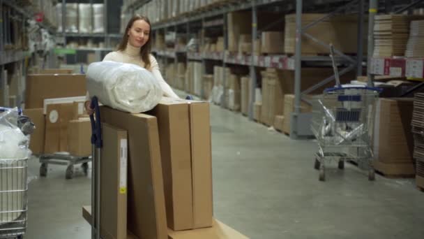 No armazém, uma mulher dirige um carrinho de compras e seleciona mercadorias — Vídeo de Stock