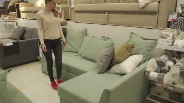 Cliente feminino escolhendo sofá no centro comercial. Mulher sentada no sofá imaginando seu novo arranjo arquitetônico em casa. — Vídeo de Stock