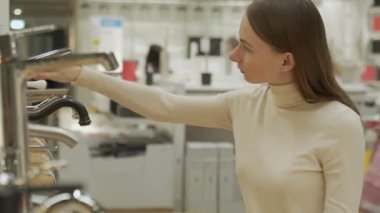 Kadın, bir ev aletleri dükkanının mutfağındaki lavabo için yeni bir musluk seçiyor.