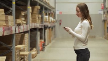 Depodaki envanteri kontrol etmek için akıllı telefon kullanan bir kadın işçi.