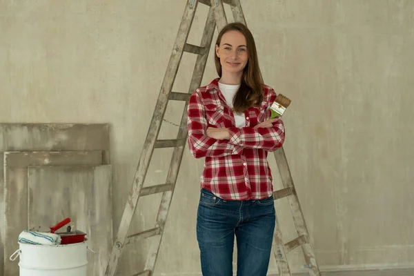 Woman paints walls at home, holds paint brush. Repair, and house renovation concept