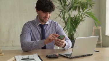 Ofiste oturup telefon kullanırken akıllı telefon kullanan bir adam. İş adamı modern ofisteki e-postaları kontrol ediyor.. 