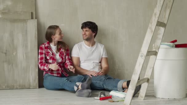 Couple familial heureux se détendre après la peinture. Jeune couple couché sur le sol de la nouvelle maison et communiquer entre eux — Video