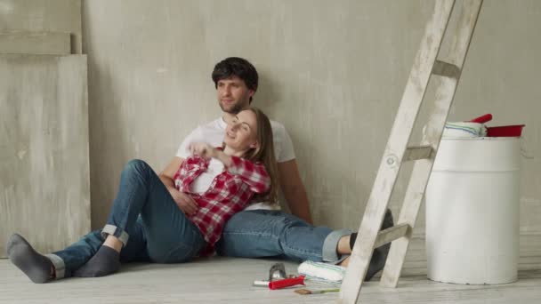 Pareja feliz familia relajándose después de pintar. Pareja joven acostada en el suelo de una casa nueva y se comunican entre sí — Vídeo de stock