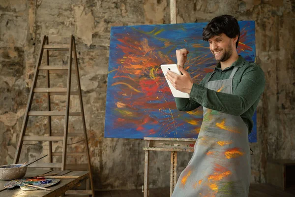 Wygrywa artysta stojący w swoim studio za pomocą tabletu. Warsztaty z malarstwem olejnym — Zdjęcie stockowe