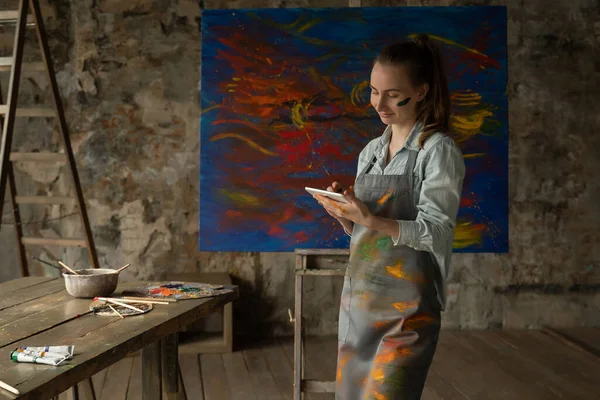 Un artista talentoso usando una tableta en el fondo de un cuadro pintado — Foto de Stock