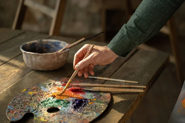 La mano dell'uomo prende un pennello dal tavolo in cui giacciono gli strumenti di disegno. — Foto Stock