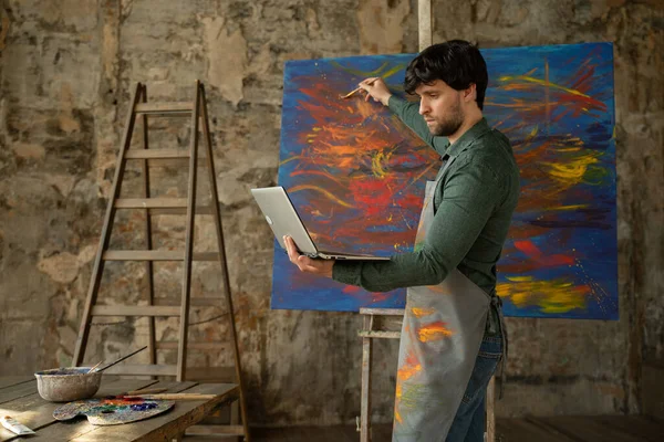 Художник-мужчина рисует картину и проводит дистанционное обучение рисованию. мужчина показывает, что она рисует и учит своих учеников — стоковое фото