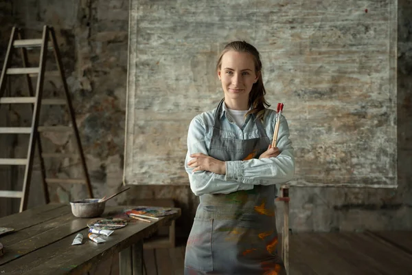 Portrait happy woman artist wearing apron looking at camera and smiling while standing in her art studio