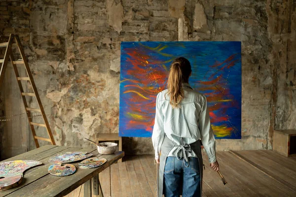 Vista posteriore artista femminile si avvicina un cavalletto con un dipinto — Foto Stock