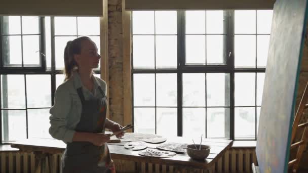 Ταλαντούχα γυναίκα καλλιτέχνης προσεγγίζει ένα μεγάλο καμβά σε ένα στούντιο τέχνης για να δημιουργήσετε ένα αριστούργημα — Αρχείο Βίντεο