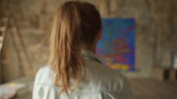 Vista posteriore artista femminile si avvicina un cavalletto con un dipinto — Video Stock