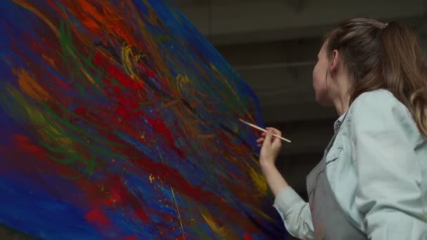Artiste dans un tablier peint un tableau sur toile avec des peintures à l'huile dans son atelier — Video