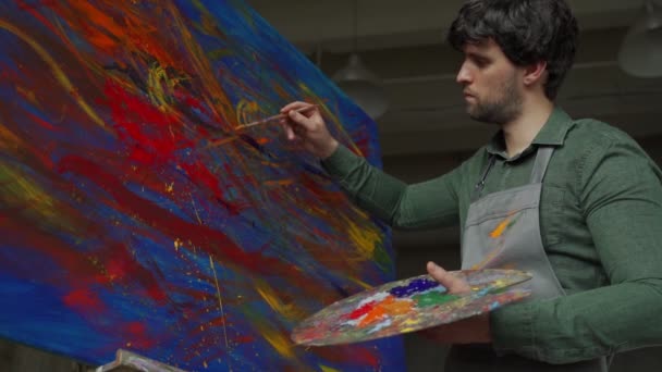 El hombre es un artista, sosteniendo un pincel y dibujando un cuadro abstracto — Vídeo de stock