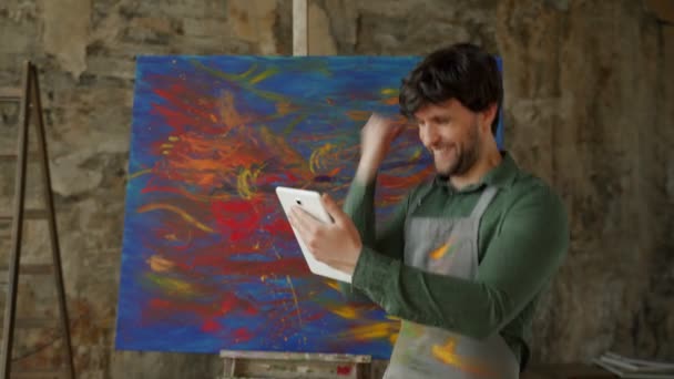 Artiste masculin debout dans son atelier à l'aide d'une tablette gagne. Atelier avec peinture à l'huile — Video