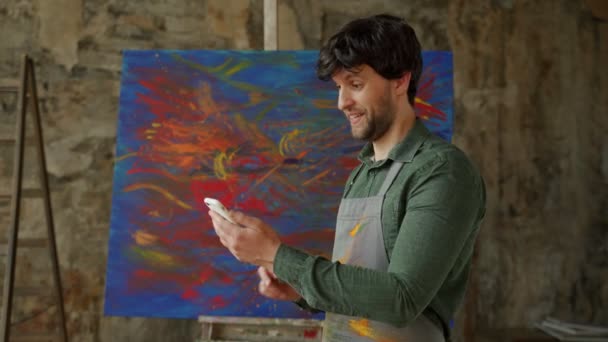 Maschio artista in piedi nel suo studio utilizzando un tablet vince. Workshop con pittura ad olio — Video Stock