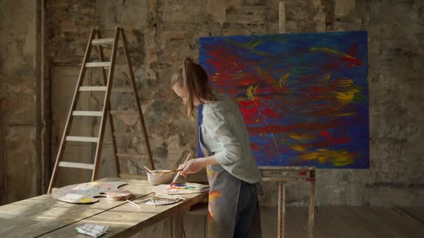 Donna artista che tiene pennello su tela di grandi dimensioni in studio d'arte. Pittura moderna su tela — Video Stock