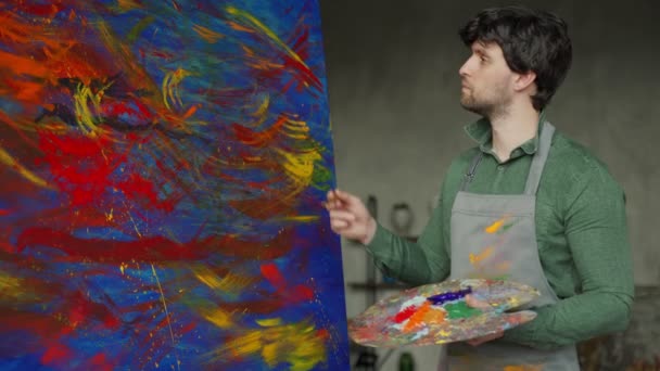 Artista masculino inspirado pone los toques finales a su pintura en un estudio brillante — Vídeo de stock