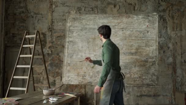 Talentoso artista masculino que trabaja en una pintura abstracta aplica trazos ligeros con un pincel — Vídeo de stock