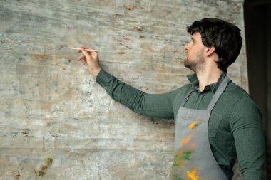 Odaklanmış erkek sanatçı resim atölyesinde resim çiziyor.